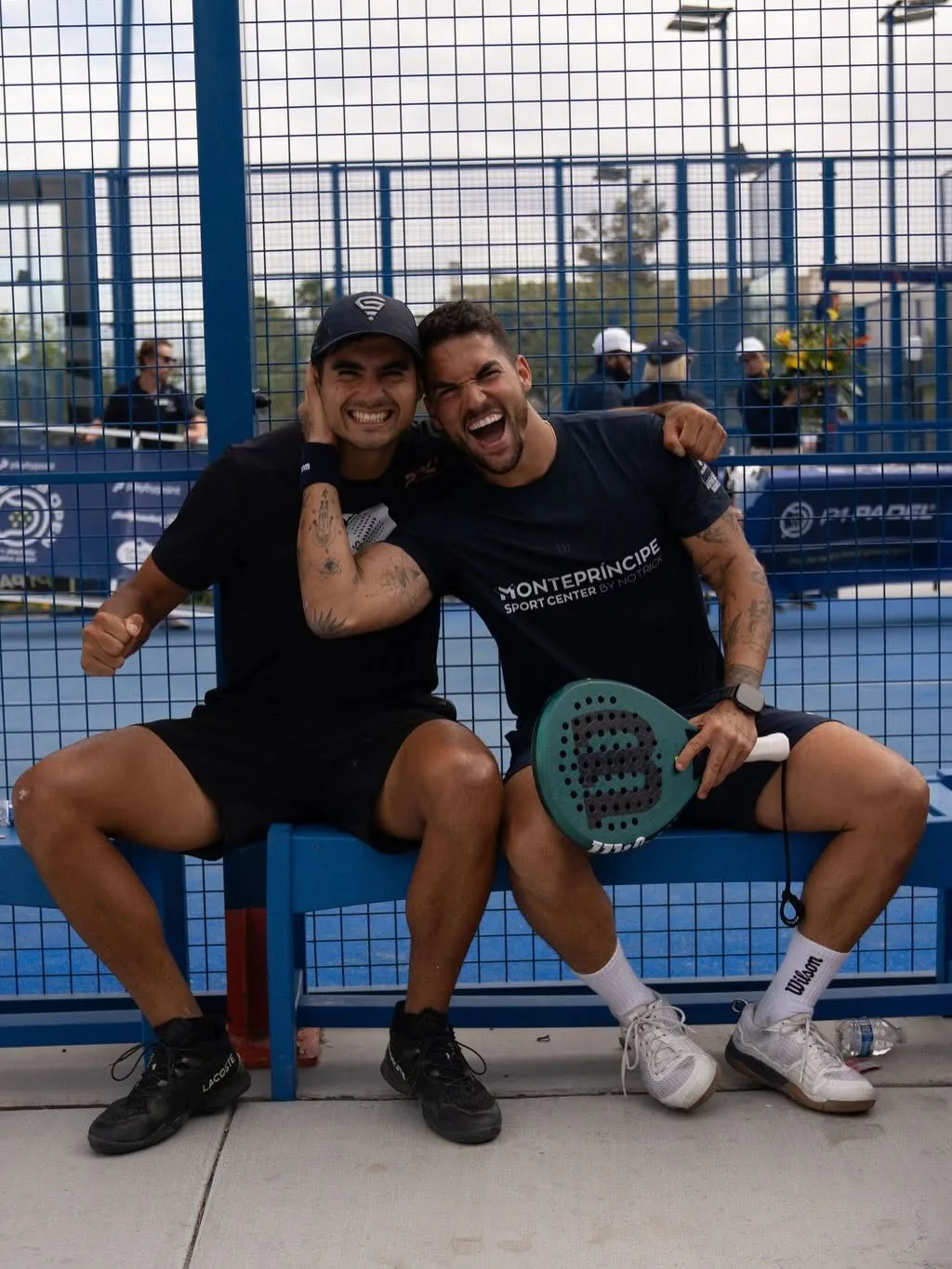 Two padel players laughing on a courtside bench at P1 Padel